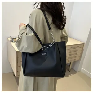 Detail of black tote bag featuring leather chain strap and embossed fashion logo plaque