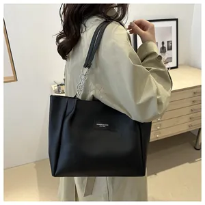 Detail of black large tote bag featuring metallic chain straps and minimalist matte leather