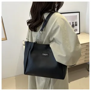 Detail of black leather tote bag featuring a silver chain strap and fashion label on the side