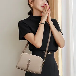 Elegant taupe litchi leather crossbody bag with dual zippers and metal buckle on a model