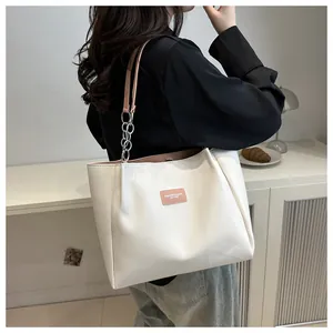 Close-up of white leather tote bag featuring a pink brand label and metal chain strap
