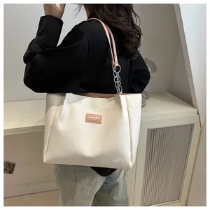 Detail of ivory tote bag featuring pink leather strap, metal chain link, and magnetic closure