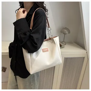Detail of cream tote bag featuring orange leather patch and silver chain strap accent