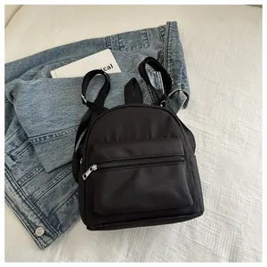 Mini mochila de nailon negro con cremalleras metálicas y correas ajustables sobre denim