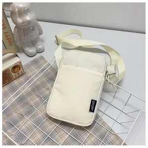 Detailaufnahme der cremefarbenen Nylon-Handytasche mit SPORT-Tag und Schultergurt