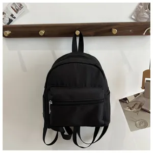 Detalle de una mini mochila de nailon negro con bolsillo frontal y herrajes plateados