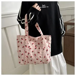 Close-up van de roze corduroy draagtas met aardbeienprint gedragen door een model