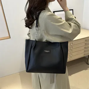 Minimalist large black tote bag with silver chain strap shown on model in trench coat