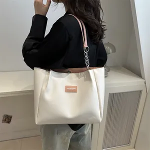 Minimalist cream tote bag with silver chain strap shown as a stylish shoulder bag on model