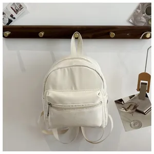 Detalle de una mochila pequeña de lona impermeable color crema colgada en gancho de madera