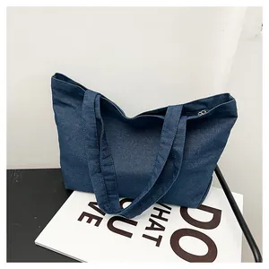 Detail of dark blue denim tote bag showing reinforced straps and top metal zipper