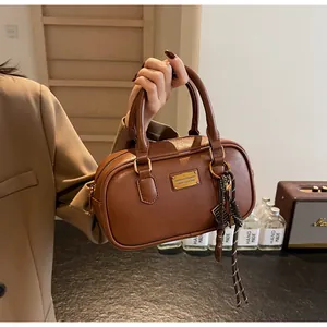 Nahaufnahme einer braunen Lederhandtasche mit goldener Plakette und gestreiftem Anhänger