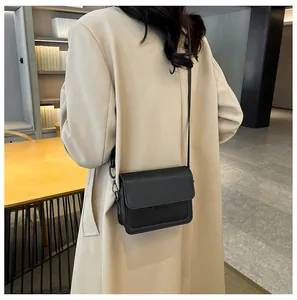 Detail of minimalist black leather square bag with flap closure and slim shoulder strap