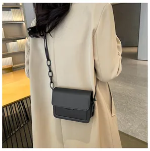 Chic black crossbody flap bag with chunky chain strap on beige coat lifestyle view