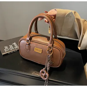 Detailansicht einer braunen Leder Boston Bag mit goldenem Emblem und gewebtem Anhänger