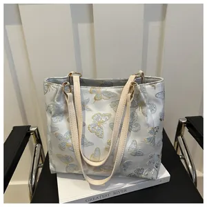 Detail of blue tote bag with butterfly embroidery and off-white faux leather straps