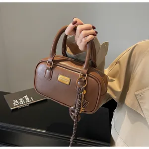 Detailansicht einer braunen Vintage-Boston-Tasche mit Goldplakette und Web-Anhänger