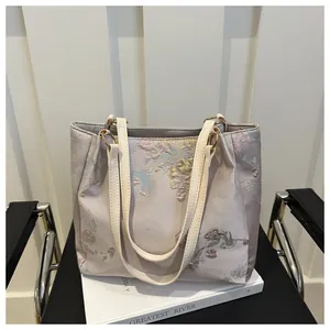 Detail of floral embroidery on a purple satin tote bag with leather handles