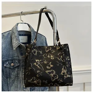 Detail of the golden butterfly print on a black velvet tote bag hanging on a rack