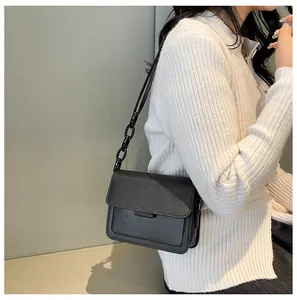 Detail shot of a black textured crossbody bag with chain strap on a model shoulder