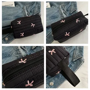 Detail view of black quilted makeup bag with pink bow embroidery and sturdy zipper strap