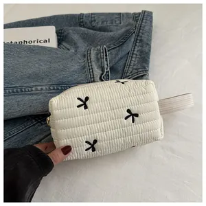 Detail of white quilted cosmetic bag with black embroidered bows and woven handle