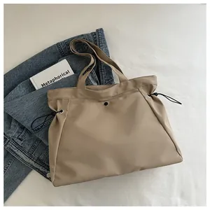 Detail of khaki nylon tote bag featuring adjustable black side drawstrings and shoulder strap