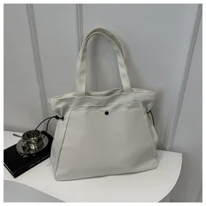 Detail view of cream nylon tote bag with black button and drawstring on white display