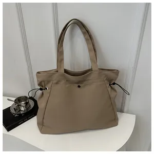 Detail of khaki nylon tote bag with side drawstring and front snap pocket on display