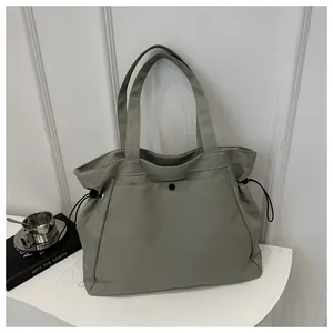 Detail of grey-green tote bag showing side drawstrings and large front button pocket