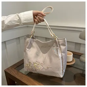 Close-up of floral and butterfly embroidery on a beige silk-textured tote bag