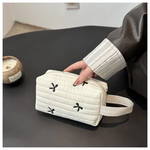 Macro view of cream quilted makeup bag with black bow embroidery and fabric handle