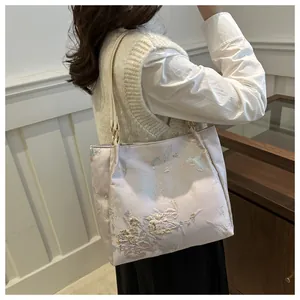 Detail of embroidered butterfly floral patterns on a satin texture tote bag worn by a model