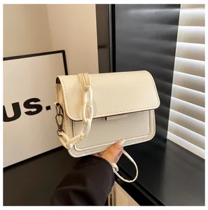 Detail of cream crossbody bag with acrylic chain and adjustable strap in natural light