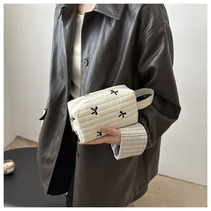 Quilted cream cosmetic bag featuring black bow embroidery and convenient strap handle
