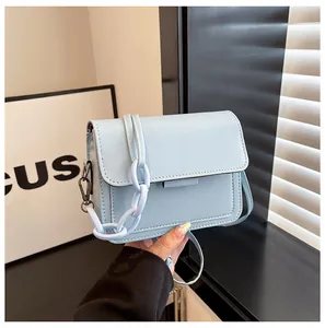 Detail of light blue crossbody bag with textured leather, flap cover and metal chain strap