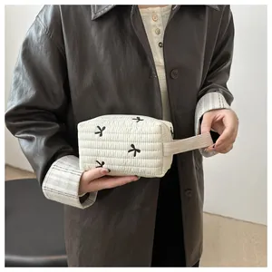 Close-up of quilted white makeup bag with black bow embroidery and woven handle