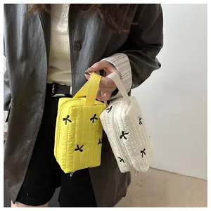 Detail of yellow and beige quilted makeup bags with delicate black bow embroidery