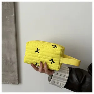 Detailed shot of yellow quilted cosmetic bag featuring black floral embroidery and wide handle