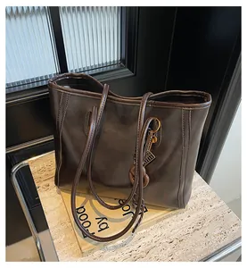 Detail of a dark brown glossy leather tote bag with a heart charm on marble background