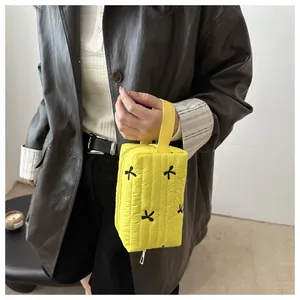 Close-up of a yellow quilted makeup bag with black butterfly embroidery and top handle