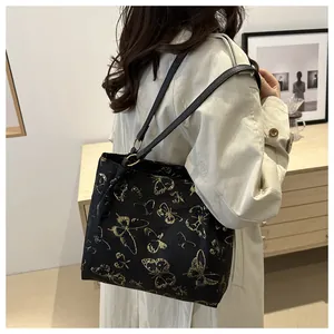 Large black shoulder tote bag with golden butterfly pattern worn over a beige trench coat