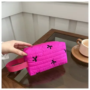 Macro detail of fuchsia quilted makeup bag with black bow embroidery and strap handle