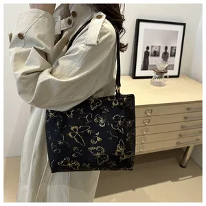 Detail of black tote bag featuring gold butterfly embroidery and slender shoulder straps