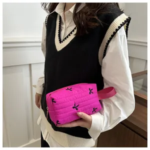 Detail of rose red quilted cosmetic bag with black bow embroidery and side strap