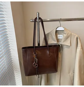 Detailed shot of dark brown tote bag with metal charms on a minimalist coat rack