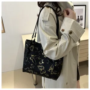 Detailed shoulder view of large black tote bag with gold butterfly print on model