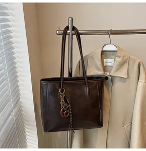Detail of dark brown faux leather tote with bronze key pendant and neat stitching
