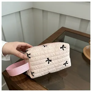 Pink quilted cosmetic bag with black embroidered bows and fabric carry handle detail
