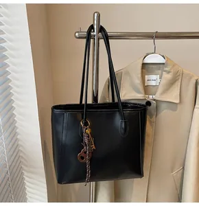 Detail of black leather tote bag with a decorative brown heart pendant and braided charm